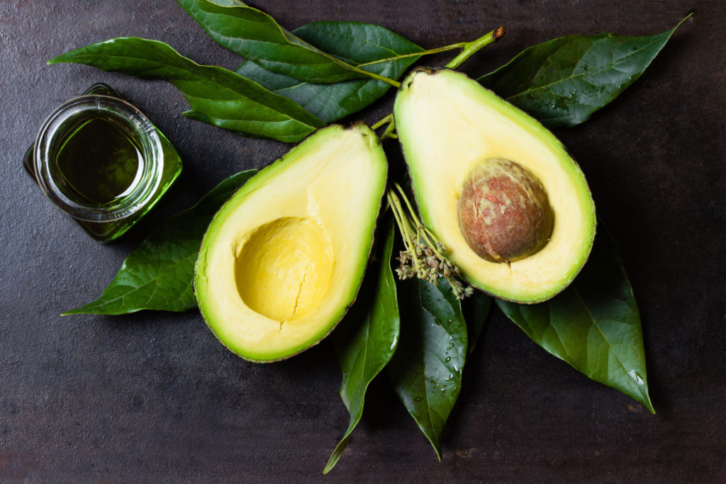 Avocado cut in half with leaves and avocado oil