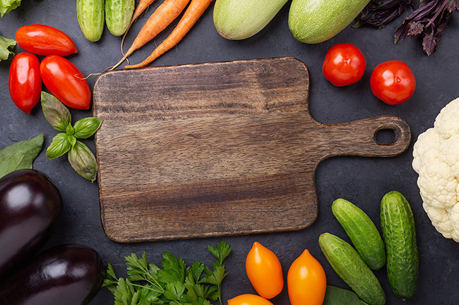 Wooden cutting board surrounded by vegetables. 