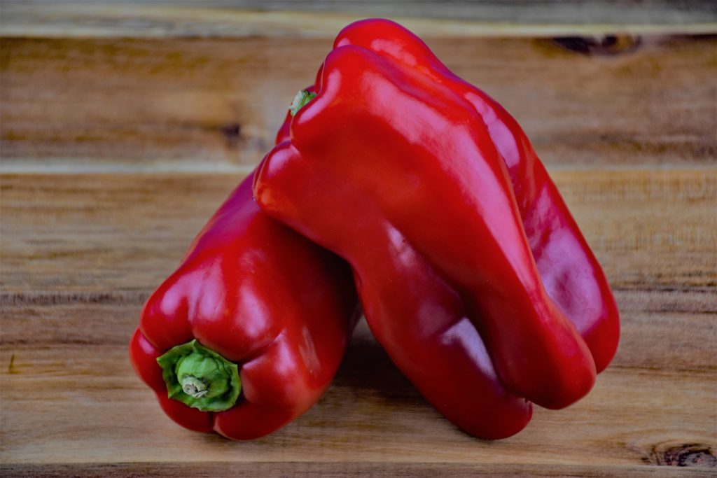 Two red bell peppers on a wooden cutting board